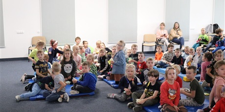 Powiększ grafikę: Dzieci siedzą na podłodze w auli szkolnej czekają na seans filmowy