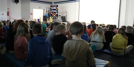 Powiększ grafikę: Uczniowie siedzą  w auli szkolnej przed seansem filmowym