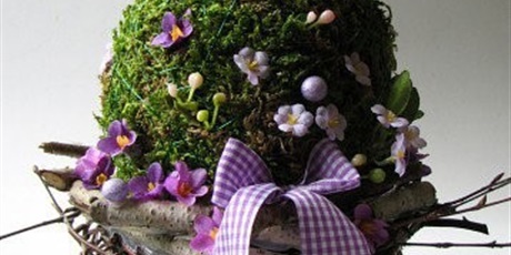 Powiększ grafikę: Zdjęcie stroika w kształcie jajka pokryte mchem i filetowymi kwiatami. Na górze stoi figurka szarej myszki