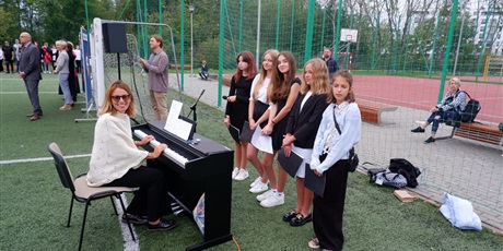 Powiększ grafikę: Szkolny chór podczas rozpoczęcia roku szkolnego: nauczycielka muzyki przy pianinie i pięć dziewcząt z chóru szkolnego.