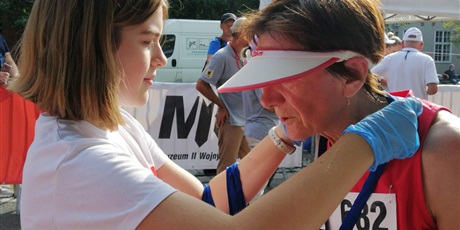 Powiększ grafikę: Uczennica wiesza medal na szyki jednego z uczestników biegu