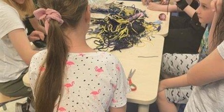 Powiększ grafikę: Dzieci przy stoliku pletą makramy z kolorowych sznurków