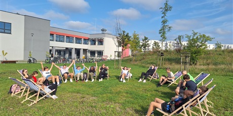 Powiększ grafikę: Uczniowie siedzą na leżakach na trawniku szkolnym.