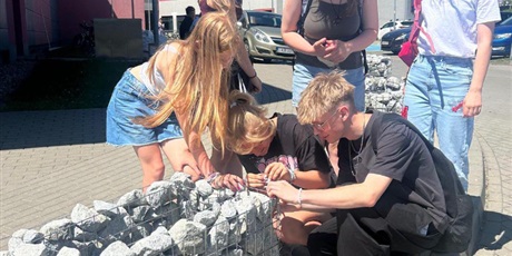 Powiększ grafikę: Uczniowie mocują tabliczkę na kamiennej donicy