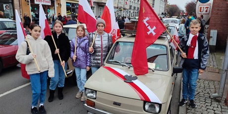 Powiększ grafikę: Uczniowie z fagami stoją przy "małym "fiacie z godłem polski i flagą na masce