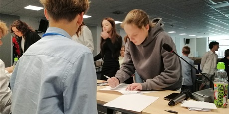 Powiększ grafikę: Uczniowie przy stole podpisują karty