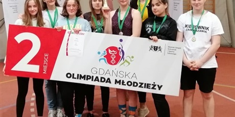 Powiększ grafikę: Nagrodzone uczennice z medalami  trzymają transparent  promujący zawody Gdańskiej Olimpiady Młodzieży