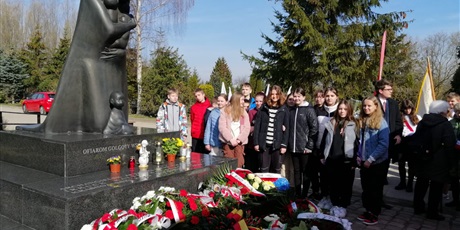 Powiększ grafikę: Uczniowie stoją przy pomniku z kwiatami