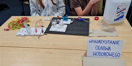 Powiększ grafikę: Uczniowie podczas warsztatów stoją przy jednym ze stołów z eksperymentem.