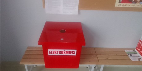 Powiększ grafikę: Czerwony kontener na elektrośmieci zakupiony przez Rade Rodziców stoi na ławce w przedsionku wejścia do budynku C