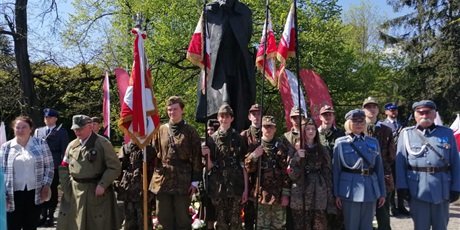 Powiększ grafikę: Uczniowie w mundurach harcerskich z flagami stoją na tle pomnika Józefa Piłsudskiego